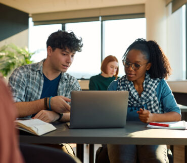 Multiracial students e-learning over a laptop at university classroom.